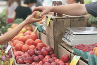 Two hands holding an apple over a fruit stand